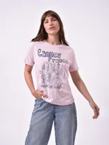 Remera blanca de algodón con cuello redondo y manga corta. Presenta un pequeño bordado en el pecho izquierdo con una figura que parece ser una persona acostada en una tabla de surf o flotador.