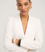 Blazer blanco de corte sastre, cruzado con doble botonadura de dos botones color beige. Presenta solapas de muesca y bolsillos de ojal con tapa en la parte delantera.