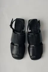 Sandalias negras de cuero con diseño de tiras entretejidas, puntera cuadrada, tira trasera con hebilla ajustable y tacón bajo cuadrado.
