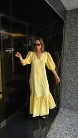 Vestido largo color amarillo pálido, con escote en V, mangas cortas abullonadas con detalle de calado y ruedo con volantes y calado.