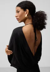 Vestido largo negro de mujer con manga japonesa, cuello caja en delantero y escote en espalda con nudo. Ajuste en cadera con godets y bajo asimétrico.