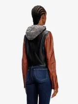 Chaqueta de cuero de oveja negra con mangas marrones y capucha de algodón gris extraíble con cordones. Cierre frontal con cremallera, cuello alto minimalista, puños con cremallera y forro interior.
