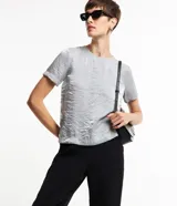 Blusa plateada de mangas cortas con cuello redondo pespuntado, botón en la espalda y superficie metalizada.
