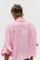 Camisa de lino a rayas verticales rosas y blancas, con cuello solapa, manga corta abullonada y lazos en los puños. Cierre frontal con botones ocultos.