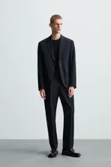 Pantalón de vestir azul marino, de corte recto, con bolsillos laterales y traseros. Se ajusta a la cintura con cinturón de cuero marrón.