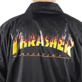 Campera negra tipo windbreaker con cuello camisero, cierre frontal con botones a presión, bolsillos laterales y logo de Thrasher en amarillo en el pecho.