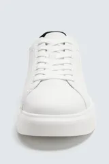 Zapatillas blancas de cuero sintético, con cordones y detalle de pieza a contraste en color negro en la parte posterior. Suela de goma blanca con volumen de diseño irregular.