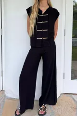 Blusa sin mangas color beige claro, confeccionada en lino tusor. Presenta cuello mao y cierre frontal con tres nudos chinos blancos. Los bordes de la abertura frontal tienen un acabado deshilachado.