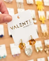 Par de aros Valente con aro dorado y dije de flor color ámbar. El diámetro del aro es de 1,5 cm y el diámetro de la flor es de 1,5 cm. El aro es de acero y la flor es de acrílico.