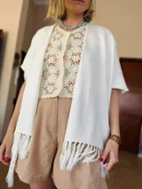 Ruana tejida color crudo con flecos en los bordes. Diseño abierto y corte rectangular.