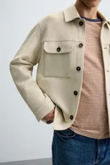 Sobrecamisa color beige de tejido efecto ante, corte regular fit, con cuello solapa, manga larga con puños abotonados, bolsillos de parche con solapa en el pecho y bolsillos de ojal en la cadera.