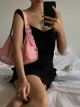 Cartera negra de lona semi impermeable con cierre metálico, forrería de gross y bolsillo interno. Tiene tira regulable y etiqueta blanca con texto en el frente.