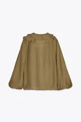 Camisa color verde oliva de tela traslúcida, con escote en V y volantes en el frente y cuello. Mangas largas abullonadas con puños elásticos.