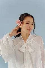 Blusa blanca de algodón con cuello alto fruncido y lazo al frente, mangas largas acampanadas.