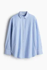Camisa Oxford de algodón a rayas verticales celestes y blancas, con cuello clásico, botones frontales, corte holgado, mangas largas con puños abotonados y bajo redondeado.