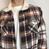 Chaqueta de franela a cuadros en tonos marrón, blanco, azul y naranja, con cuello de corderito blanco, cierre con botones a presión, bolsillos en el pecho con solapa y bolsillos laterales.