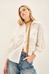 Camisa blanca de algodón con bordado de corazones dorados, corte amplio, cuello clásico, cartera con botones ocultos y bolsillo en el pecho.