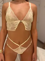 Conjunto de lencería color champagne de encaje floral, compuesto por un corpiño tipo top con breteles regulables y cierre frontal, y una tanga regulable de tiro alto con corte medialess.