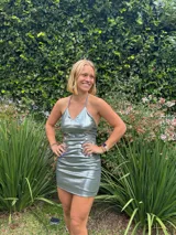 Vestido corto ajustado color plateado metalizado, con escote en V y tirantes finos que se cruzan en la espalda semi baja.