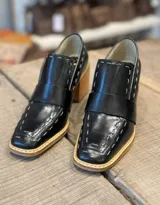 Mocasines negros de cuero con tacón de madera, puntera cuadrada y detalle de costuras en contraste.