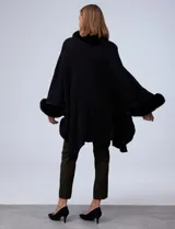 Ruana o poncho negro de tejido suave, con cuello y puños adornados con apliques de piel sintética (faux fur).