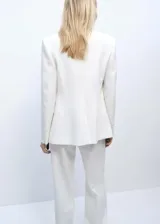 Traje sastrero blanco de tres piezas, compuesto por blazer con solapas de muesca y cierre de un botón, chaleco con escote cuadrado y doble botonadura, y pantalón de corte recto y bota ancha.