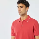 Chomba de piqué color rojo con cuello clásico y borde blanco, de corte recto y manga corta.