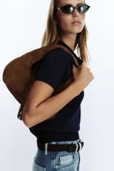 Bolso de hombro marrón de serraje con asa corta y flecos decorativos.