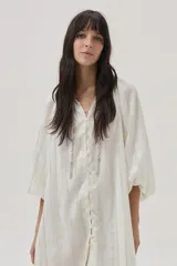 Vestido corto color crudo con rayas verticales plateadas, de manga larga abullonada y abotonado desde el escote hasta el bajo.