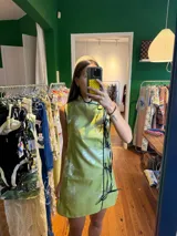 Vestido corto color verde lima con estampado floral blanco, corte cheongsam, cuello mao, sin mangas, con ribete negro y lazos decorativos en el lateral.