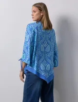 Blusa de gasa estampada marca Ruby Rd, de color azul. Tiene cuello a la base, escote en V y abertura central con botones. La delantera es plisada. Las mangas son ¾ con frunce. El ruedo y la espalda son asimétricos.