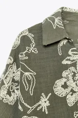 Camisa verde militar con bordado floral blanco, cuello solapa, escote en pico, manga tres cuartos con detalle de guipur y cierre frontal con botones.