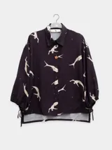 Camisa negra con estampado de figuras humanas blancas, cuello clásico, cierre frontal con botones y mangas 3/4 con lazos ajustables en los puños.