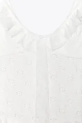 Top blanco de encaje con escote en pico, tirantes con volantes y lazo ajustable en el centro del pecho.