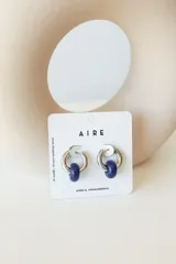 Aros de acero quirúrgico hipoalergénico con forma de argolla plateada y dije circular colgante de piedra natural color azul.