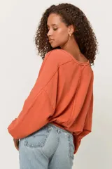 Buzo color beige de corte holgado con cuello redondo y mangas abullonadas. Presenta detalles sin rematar en la parte delantera y trasera, y detalles acanalados en las mangas y el dobladillo.