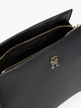 Cartera bandolera negra con textura granulada, correa ajustable y logo metálico dorado de Tommy Hilfiger en el frente.