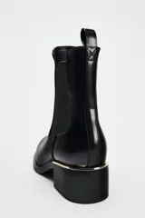 Botín Chelsea de cuero negro con elásticos laterales, puntera redondeada y detalle de placa metálica dorada en el tacón.