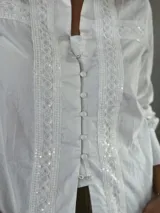Camisa blanca de corte clásico con detalles de encaje en el frente y mangas largas con puños abotonados.