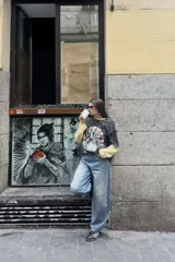 Remera de manga corta, color gris oscuro con efecto lavado, con un estampado frontal que incluye un diseño de planta en una maceta decorada, serpientes y texto. Se usa superpuesta a una remera de manga larga a rayas amarillas y blancas.