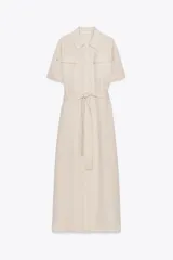 Vestido camisero largo color beige, de manga corta y cuello solapa. Tiene bolsillos de parche en el pecho, bolsillos laterales ocultos y cinturón de la misma tela.