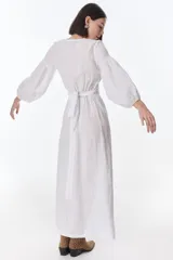 Vestido color beige de lino, con escote en V, mangas largas abullonadas y lazos frontales. Tiene corte a la cintura y falda larga con tajo frontal.