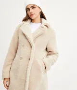 Saco alargado color beige de sherpa con cuello solapa, manga larga y abotonado delantero.