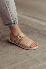 Sandalias bajas doradas de cuero, con dos tiras anchas en el empeine y hebilla lateral ajustable.