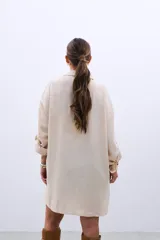 Camisa color beige con bordado de lentejuelas doradas en los hombros, corte clásico, cuello camisero y mangas largas con puños abotonados.