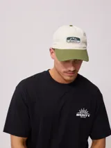 Gorra de lona lavada color beige con visera verde y parche con el logo de Rusty en el frente.