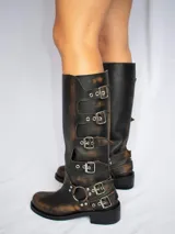 Botas de cuero gastado color marrón con hebillas y apliques de metal de caña alta.