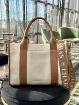 Bolso tote color crema con detalles en cuero marrón. Tiene doble asa de mano y correa de hombro extraíble con el logo de la marca.