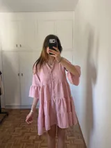 Vestido corto de silueta amplia, confeccionado en polina melange, con escote en V, botones al frente y recortes con volados. Las mangas son 3/4 con leve volumen.