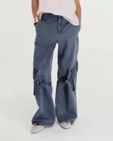 Pantalón cargo de gabardina gastada de lino y algodón color azul. Silueta de pierna recta ancha, con cartera con cierre metálico y broche níquel en el cruce de la cintura. Tiene bolsillos inclinados en los laterales y bolsillos cargo con tapa y broches metálicos a la altura de las rodillas, de los cuales salen unas tiras que se ajustan mediante hebillas metálicas para modificar la silueta del pantalón. En la espalda tiene pinzas y un bolsillo plaque con cierre metálico en boca. Es tiro medio.